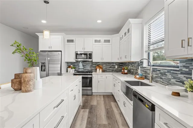 a kitchen with stainless steel appliances kitchen island granite countertop a refrigerator a sink dishwasher a stove with white cabinets and wooden floor