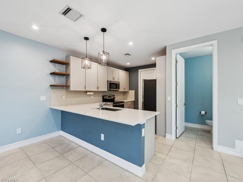 7591 Morgan Way Naples, FL 34119 - Photo 4 of 27 Kitchen with hanging light fixtures, stainless steel appliances, kitchen peninsula, and white cabinets