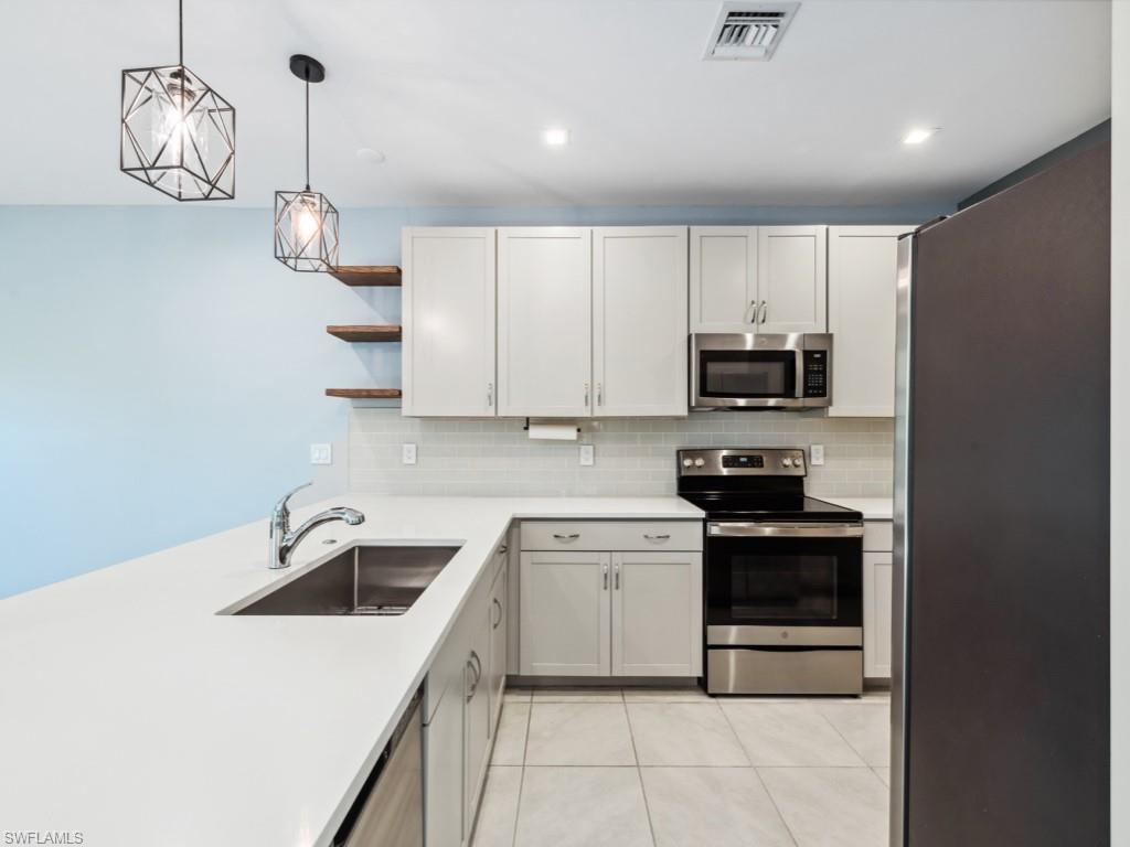 7591 Morgan Way Naples, FL 34119 - Photo 5 of 27 Kitchen featuring sink, white cabinetry, hanging light fixtures, light tile patterned floors, and stainless steel appliances