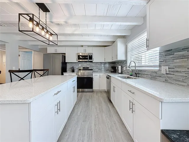 a large kitchen with stainless steel appliances granite countertop a sink dishwasher a stove top oven a refrigerator with grey cabinets and wooden floor