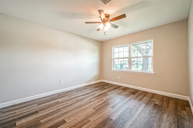 an empty room with wooden floor chandelier fan and windows