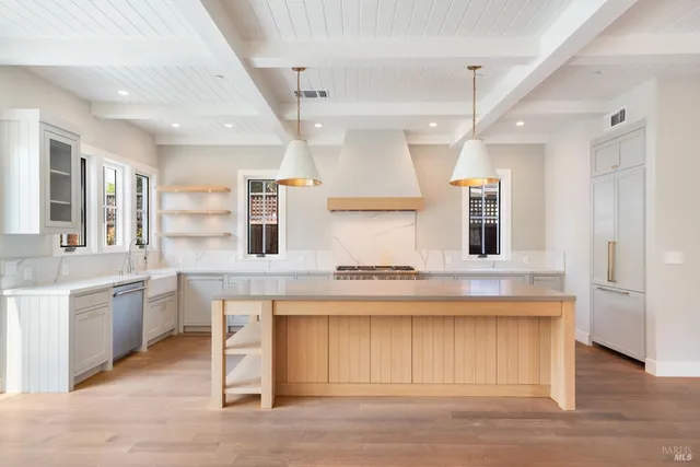 a kitchen with stainless steel appliances granite countertop a stove a sink dishwasher a refrigerator and white cabinets with wooden floor