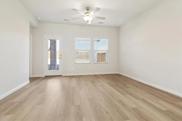an empty room with wooden floor ceiling fan and windows