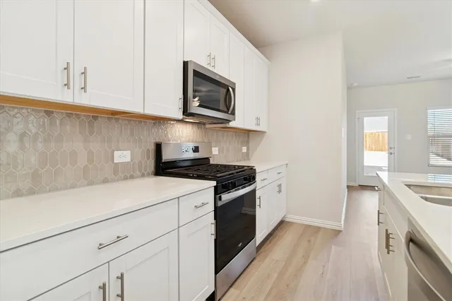 a kitchen with stainless steel appliances granite countertop grey cabinets a stove top oven and a sink