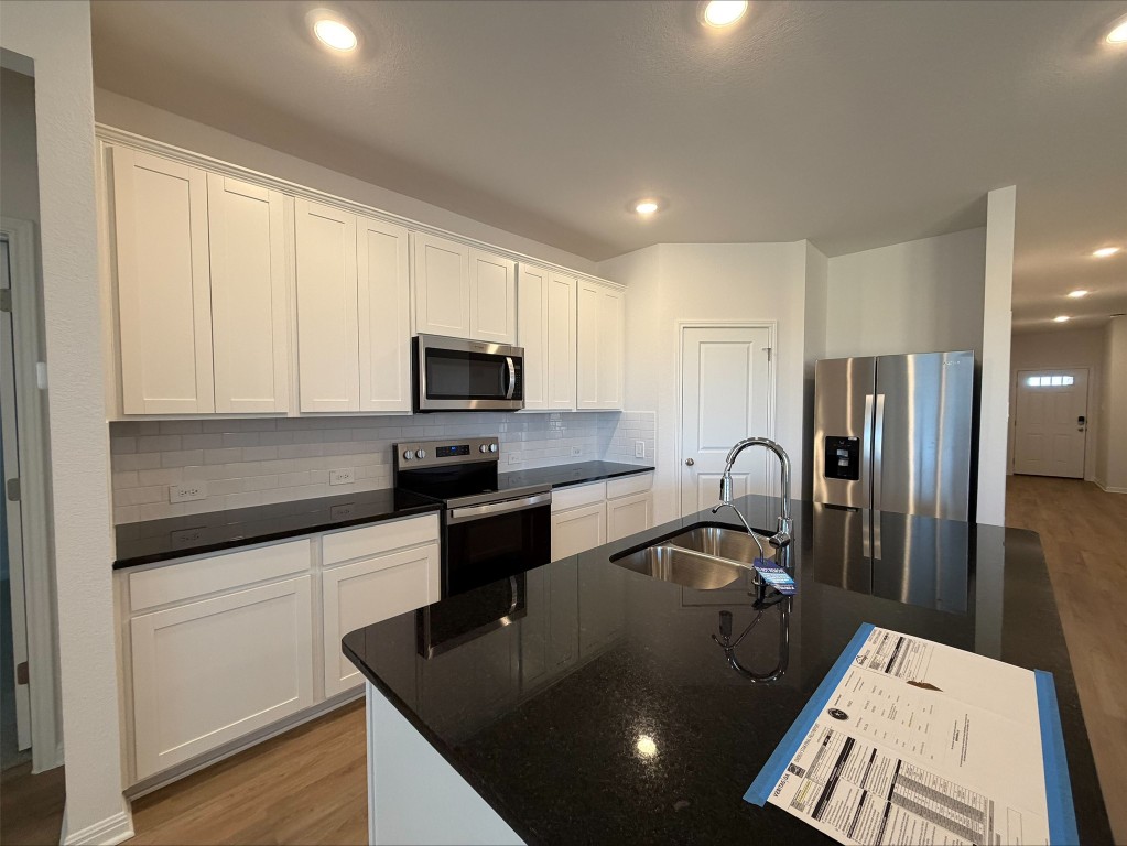 108 Honey Bee Road Jarrell, TX 76537 - Photo 7 of 9 Kitchen featuring appliances with stainless steel finishes, light wood finished floors, dark stone countertops, and recessed lighting