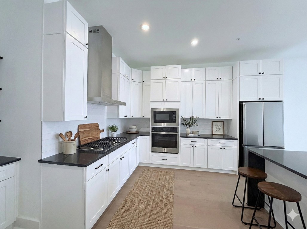 1417 Kramer Lane, Unit 20 Austin, TX 78758 - Photo 3 of 14 Kitchen with wall chimney range hood, appliances with stainless steel finishes, white cabinetry, tasteful backsplash, and a kitchen bar