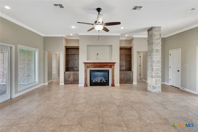 a view of an empty room with chandelier fan and fire place
