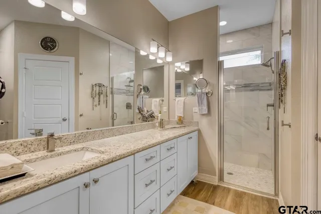 a bathroom with a granite countertop double vanity sink mirror and shower
