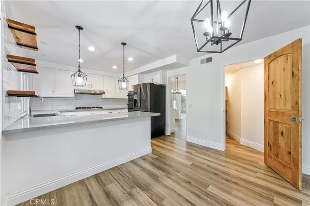 a large kitchen with stainless steel appliances granite countertop a refrigerator a oven a kitchen island with couches and wooden floor