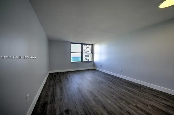 a view of an empty room with wooden floor and window