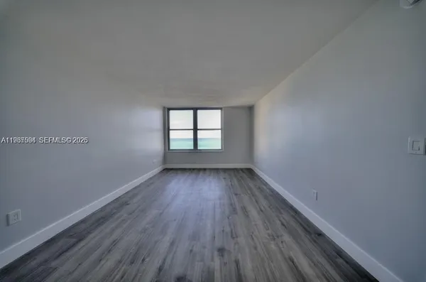 a view of an empty room with wooden floor and window