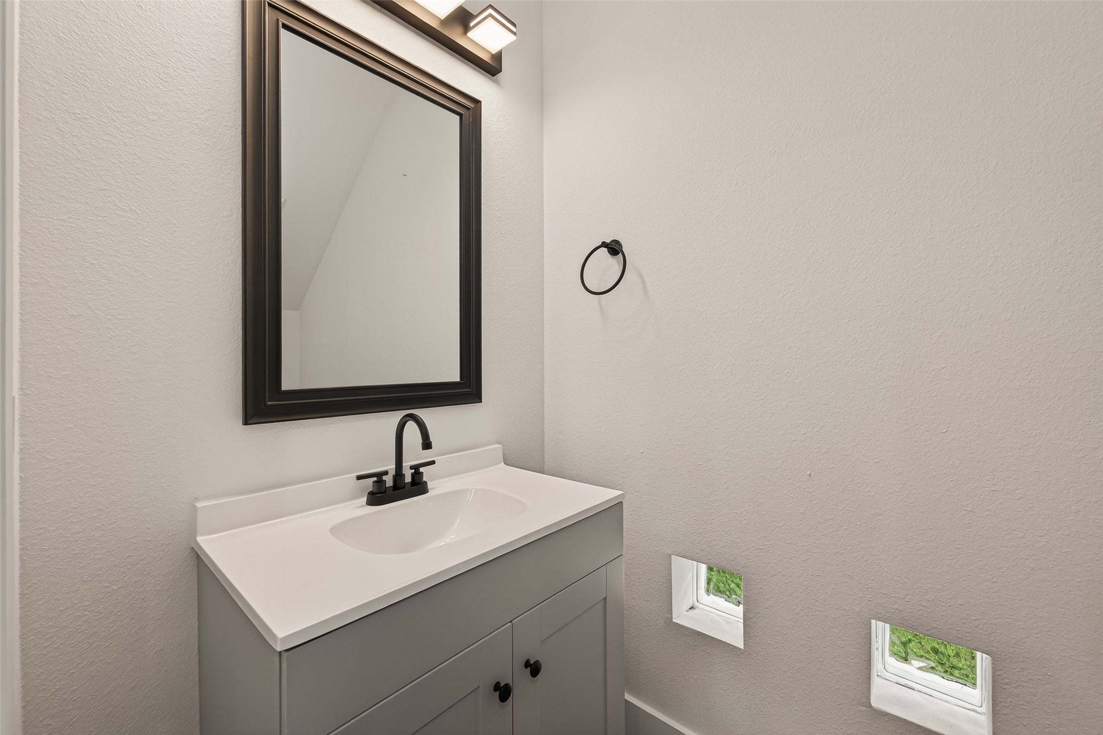6808 Madrid Street Houston, TX 77021 - Photo 15 of 31 This bathroom features a modern vanity with a sleek black faucet and a large framed mirror. The space is well-lit with contemporary lighting, and small windows provide natural light. Neutral tones create a clean and minimalist look.