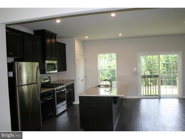 a kitchen with stainless steel appliances kitchen island granite countertop a refrigerator a stove and a wooden floor