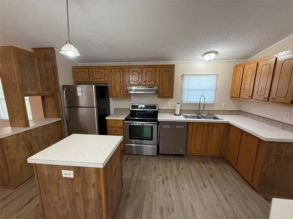 a kitchen with stainless steel appliances kitchen island granite countertop a refrigerator a sink dishwasher a stove with wooden floor and cabinets