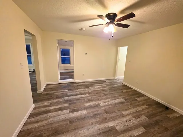 a view of an empty room with wooden floor and a ceiling fan