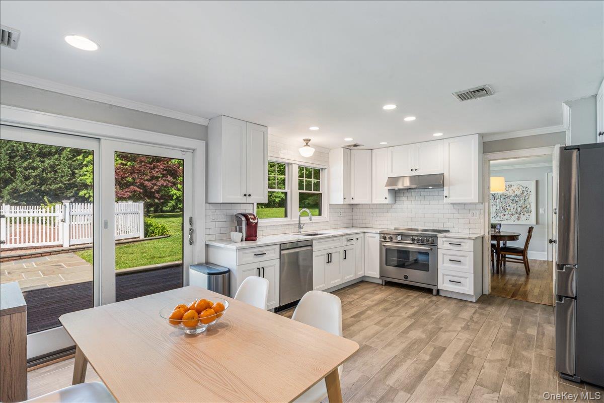 130 Sands Point Road Sands Point, NY 11050 - Photo 13 of 26 Kitchen with appliances with stainless steel finishes, under cabinet range hood, crown molding, decorative backsplash, and light countertops