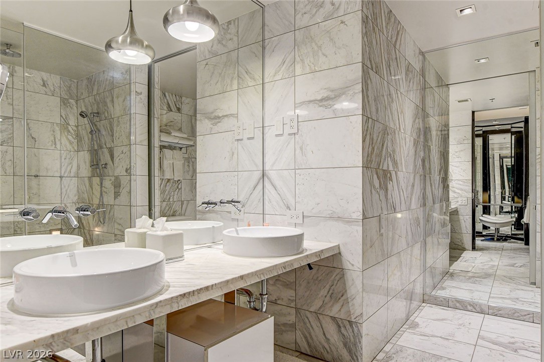 4381 West Flamingo Road, Unit 3002 Las Vegas, NV 89103 - Photo 11 of 59 Floor-to-ceiling marble tiling surrounds a floating vanity with dual vessel sinks and polished fixtures.