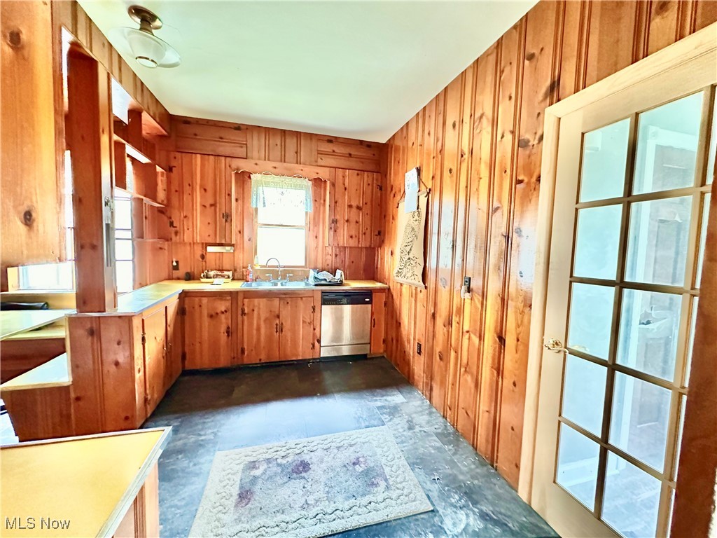 6397 King-Graves Road Fowler, OH 44418 - Photo 21 of 48 Kitchen with stainless steel dishwasher, brown cabinetry, wood walls, light countertops, and a sink