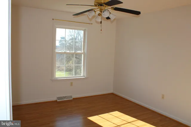 an empty room with wooden floor fan and windows