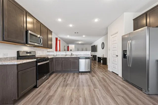 a large kitchen with stainless steel appliances granite countertop a refrigerator a stove top oven a sink and dishwasher with wooden floor