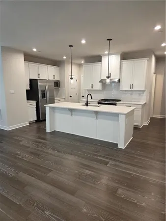 a large white kitchen with kitchen island a stove a sink dishwasher and white cabinets with wooden floor