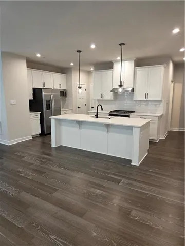 a large white kitchen with kitchen island a stove a sink dishwasher and white cabinets with wooden floor