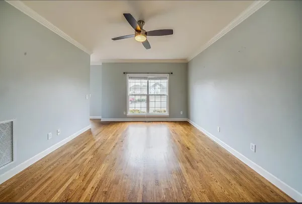 an empty room with wooden floor a ceiling fan and windows