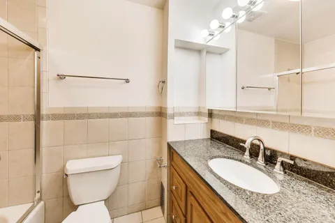 a bathroom with a granite countertop sink a toilet a mirror and shower