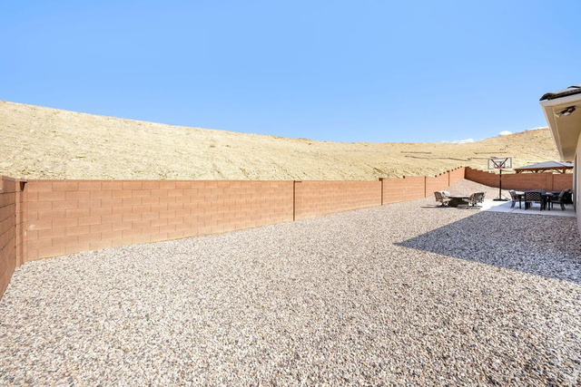 5963 Flattop Drive St. George, UT 84790 - Photo 39 of 45 Expansive gravel backyard featuring a perimeter block wall, a concrete patio area, and a basketball hoop