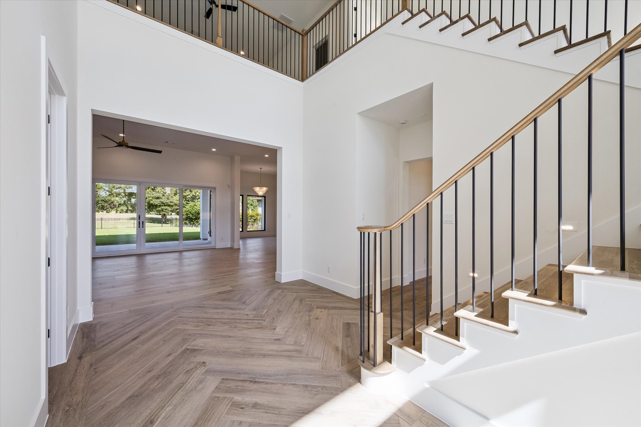 Soaring ceilings, herringbone wood-style floors, and a sleek staircase frame sunlit open-concept living.