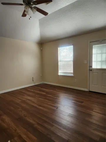 an empty room with wooden floor fan and windows
