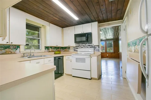 a white kitchen with a stove a sink dishwasher a microwave oven and a dining table with wooden floor