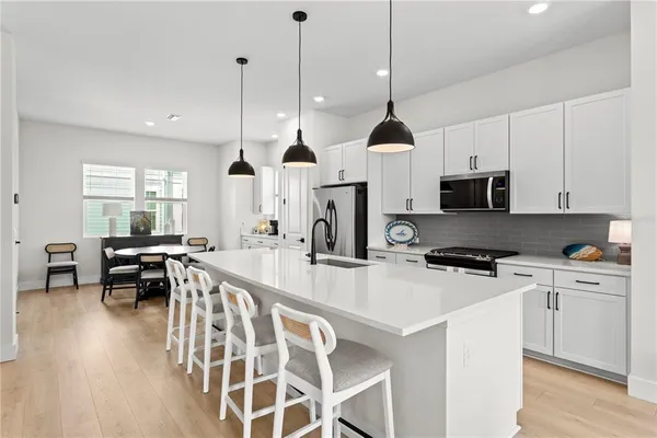 a kitchen with stainless steel appliances kitchen island granite countertop a stove a sink a microwave a dining table and chairs with wooden floor
