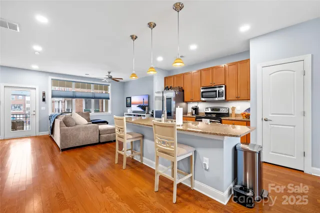 a kitchen with stainless steel appliances granite countertop a refrigerator a stove top oven a dining table and chairs with wooden floor