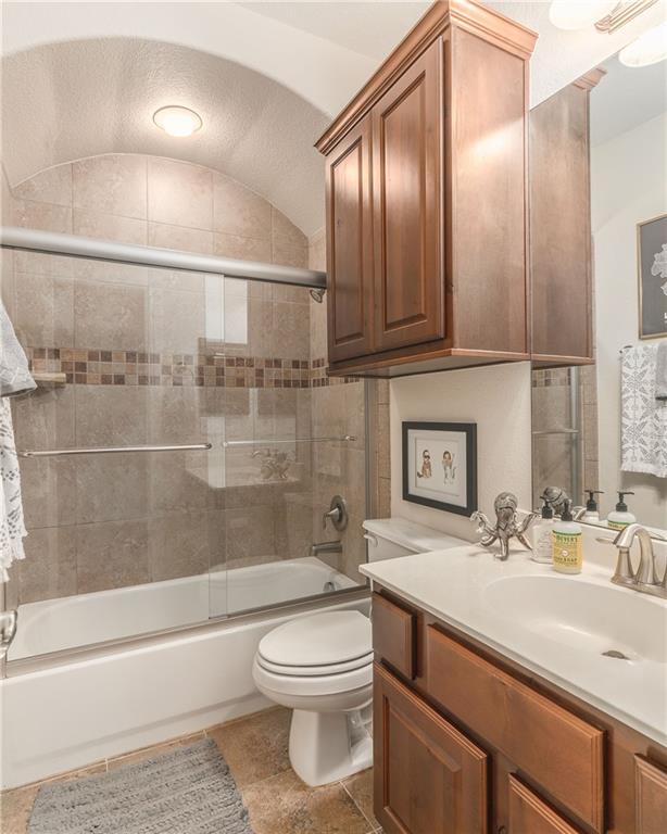 6708 Menchaca Road, Unit 14 Austin, TX 78745 - Photo 8 of 22 Bathroom featuring a built-in tub with sliding glass doors, a tile surround with decorative mosaic inlay, and an arched ceiling