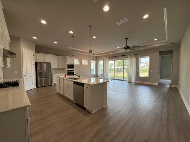 a large kitchen with stainless steel appliances kitchen island a large counter top a stove a refrigerator cabinets and living room view