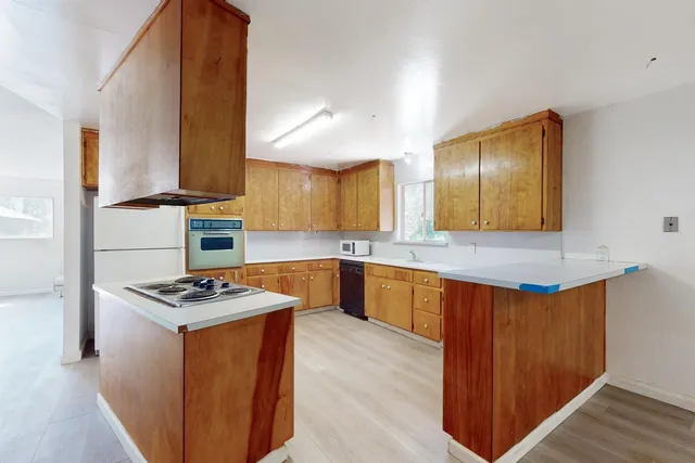 a kitchen with stainless steel appliances kitchen island granite countertop a stove a sink a refrigerator and white cabinets with wooden floor