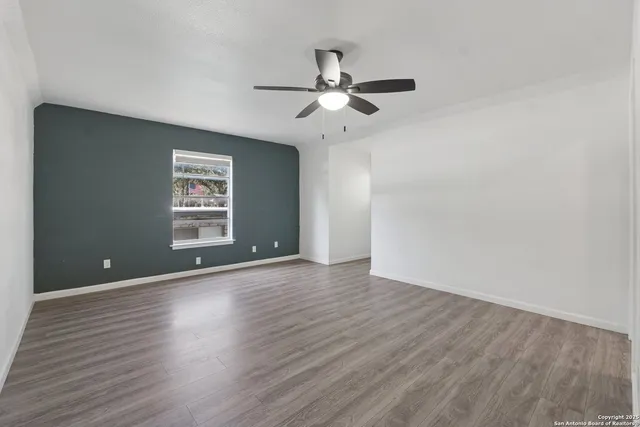 an empty room with wooden floor chandelier fan and windows