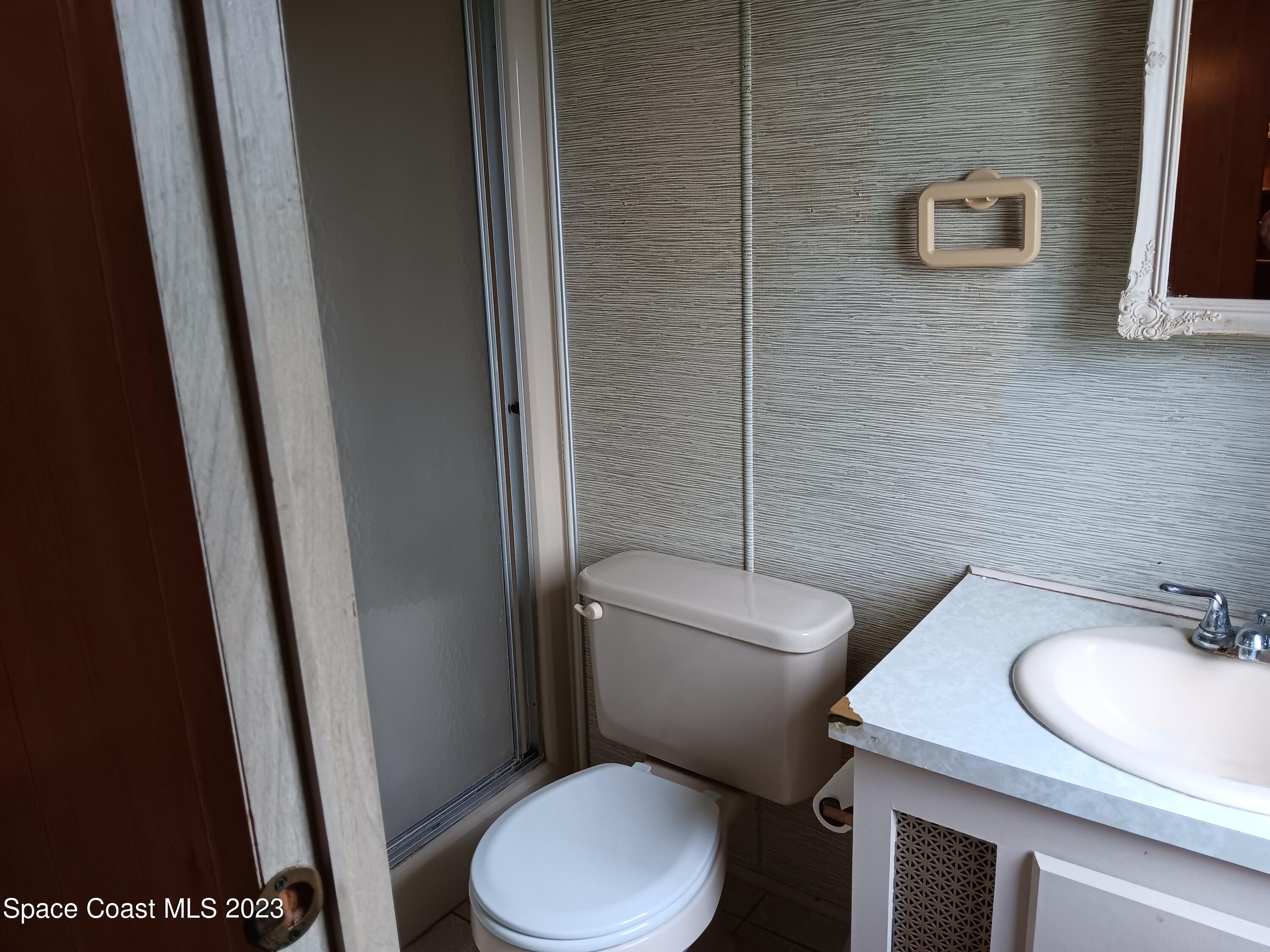 511 Puffin Drive Barefoot Bay, FL 32976 - Photo 22 of 25 a white toilet sitting next to a bathroom sink and a mirror