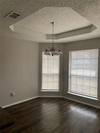an empty room with wooden floor chandelier and windows