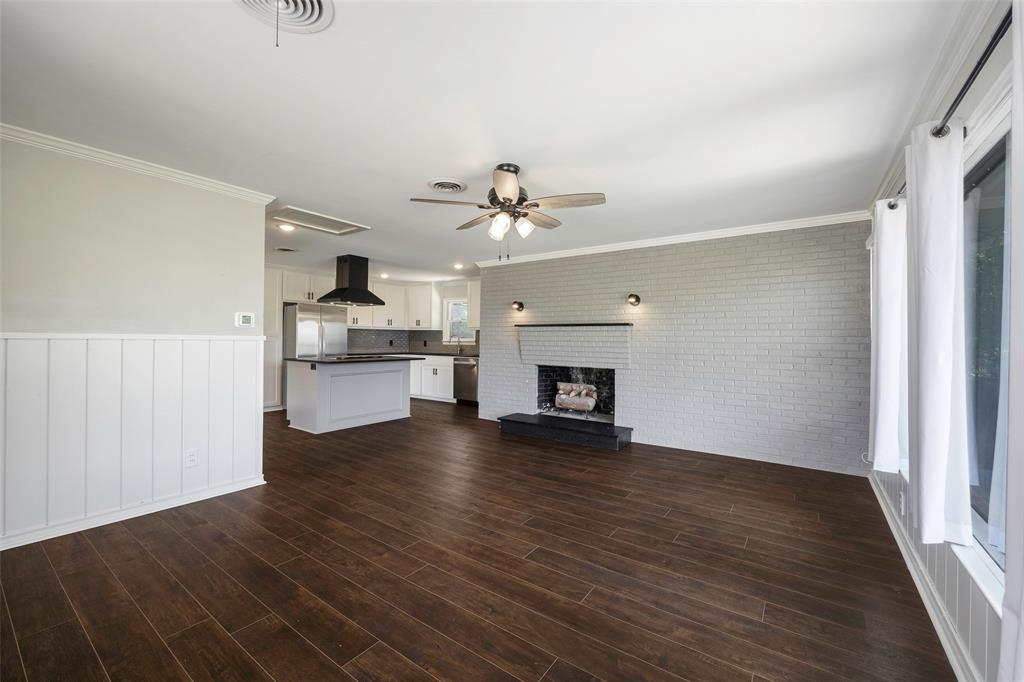 2323 Sutter Street Dallas, TX 75216 - Photo 14 of 30 Unfurnished family room featuring ceiling fan, a fireplace, dark hardwood / wood-style flooring, brick wall, and ornamental molding