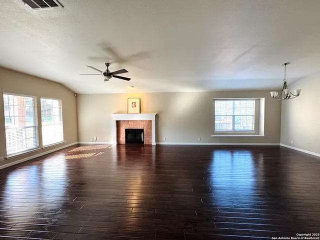 an empty room with wooden floor fireplace and windows