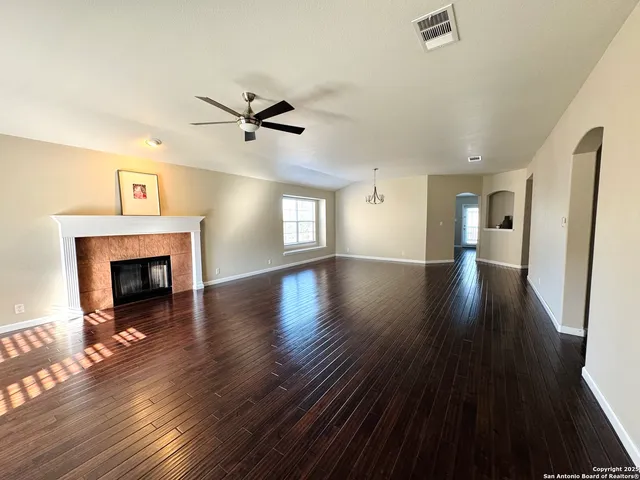 an empty room with wooden floor a ceiling fan a fireplace and windows