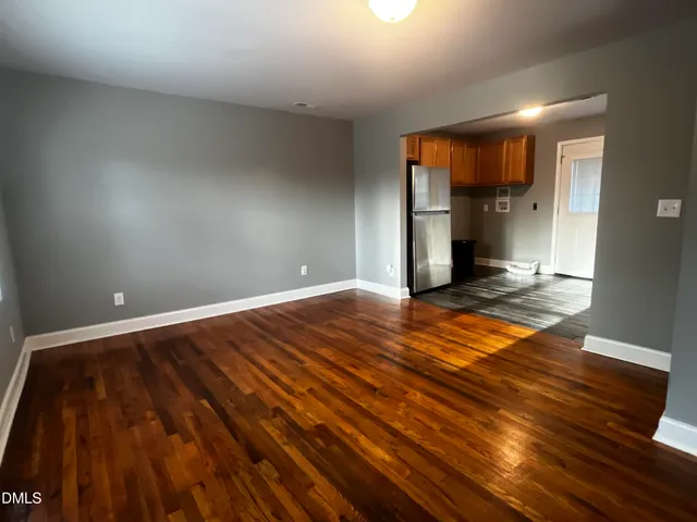 a view of empty room with wooden floor and kitchen