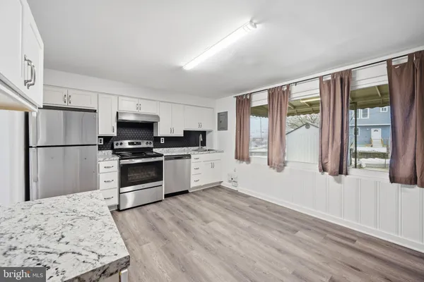 a kitchen with granite countertop a refrigerator a stove a sink and white cabinets with wooden floor