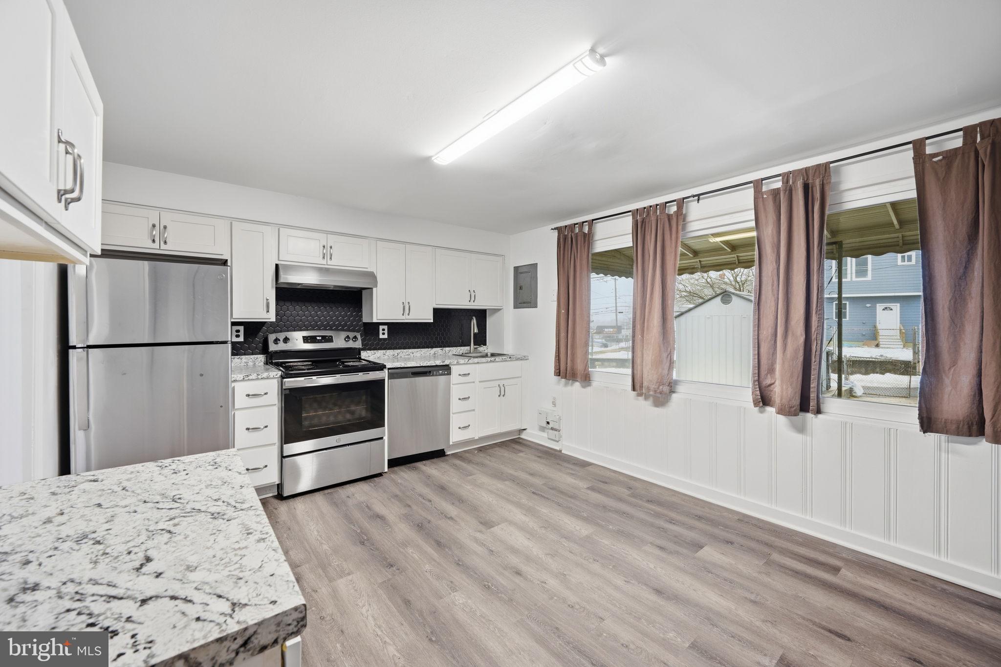 7911 Bank Street Baltimore, MD 21224 - Photo 10 of 40 a kitchen with granite countertop a refrigerator a stove a sink and white cabinets with wooden floor