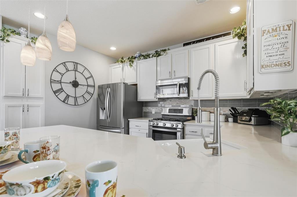 1904 Signal Ridge Place Rockwall, TX 75032 - Photo 13 of 23 Kitchen featuring white cabinets, appliances with stainless steel finishes, decorative backsplash, decorative light fixtures, and light stone countertops