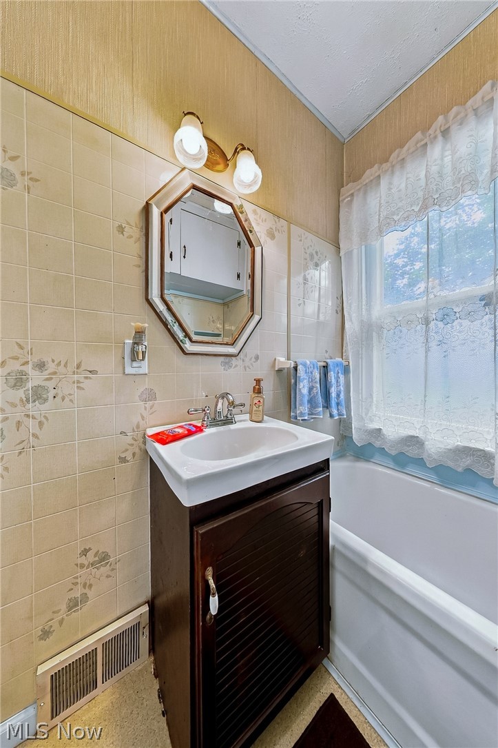 24958 Kennedy Ridge Road North Olmsted, OH 44070 - Photo 18 of 43 White porcelain sink with chrome faucet, dark wood-finish vanity, tiled walls, octagonal mirror, and wall-mounted light fixture