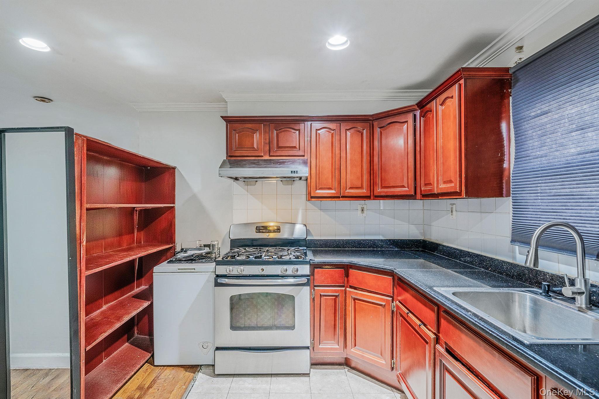 84-70 159th Street Queens, NY 11432 - Photo 21 of 50 Kitchen with stainless steel range with gas stovetop, reddish brown cabinets, backsplash, under cabinet range hood, and recessed lighting