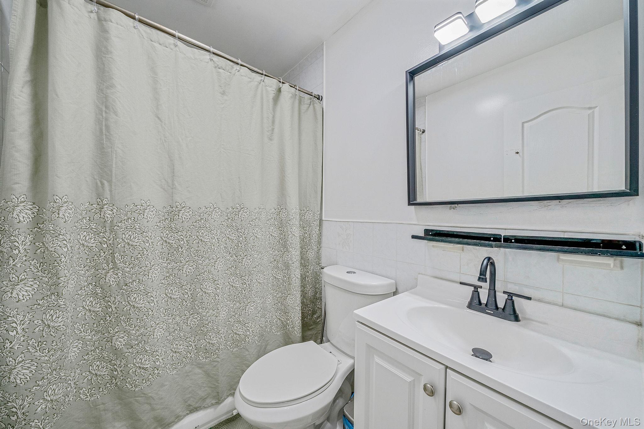 84-70 159th Street Queens, NY 11432 - Photo 25 of 50 Bathroom with vanity, a shower with curtain, tile walls, and a wainscoted wall